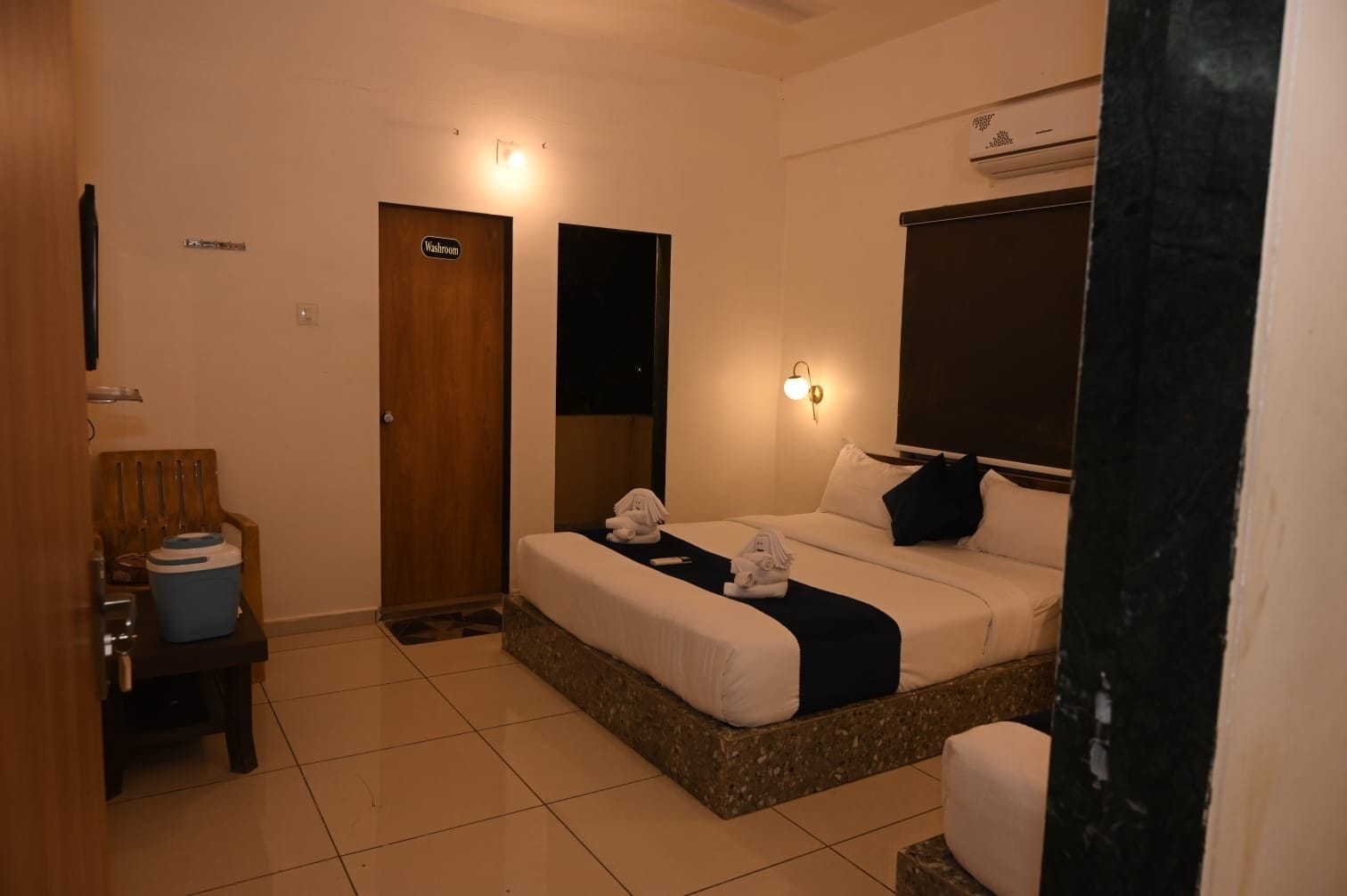 Een hotelkamer met een bed, een stoel, een nachtkastje en een bordje dat een toilet aangeeft.