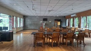 Μια αίθουσα συνεδριάσεων με ένα μεγάλο τραπέζι και καρέκλες, μια τηλεόραση και ένα παράθυρο με κουρτίνες.