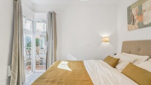 Un dormitorio con una cama grande, una ventana con cortinas, una lámpara de pared y un cuadro.