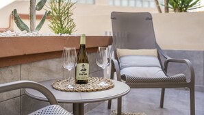 Una mesa con una botella y vasos, una silla y plantas en un patio.