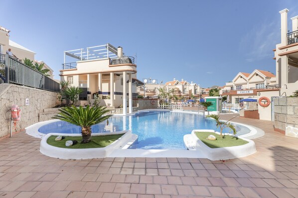 Ein Pool mit einer abgesenkten Liegefläche, umgeben von einer Ziegelterrasse, neben einem Gebäude mit Balkon.