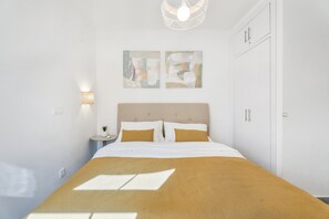 Un dormitorio ordenado con cama, mesitas de noche, cuadros en la pared y un armario.