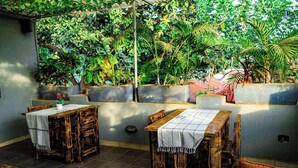 A patio with two wooden tables, each with a white tablecloth, surrounded by potted plants and a concrete wall. - Inn the woods Entebbe (Entebbe)
