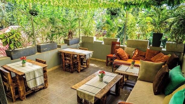 An outdoor patio area with wooden furniture, including tables and chairs, surrounded by lush greenery. - Inn the woods Entebbe (Entebbe)