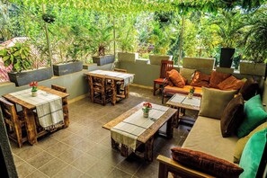An outdoor patio area with wooden furniture, including tables and chairs, surrounded by lush greenery. - Inn the woods Entebbe (Entebbe)