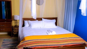 A hotel room with a bed, a nightstand, a lamp, and a mirror. - Inn the woods Entebbe (Entebbe)