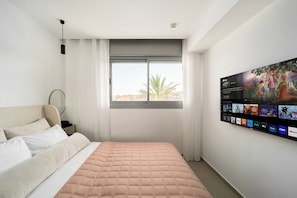 A bedroom with a bed, a window with a view, and a wall-mounted TV displaying various channels. - Red Canyon Peaceful Stay by Sea N' Rent (Eilat)