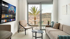 Un soggiorno moderno con una televisione a schermo piatto che mostra un programma, un divano, una poltrona e un tavolino.