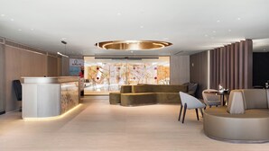 Un'area reception moderna con una scrivania a forma di arco, zona salotto con divani e poltrone, e una parete decorativa con arte astratta.