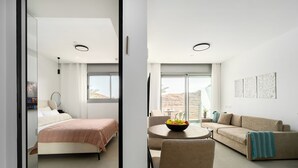 Una moderna camera d'albergo con un letto, un divano, un tavolo da pranzo con una ciotola di frutta e un'ampia finestra che si affaccia sul deserto.