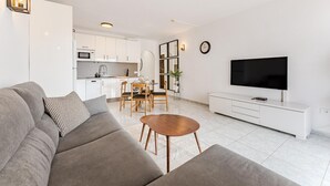 Una sala de estar moderna con un sofá, una mesa de centro, televisión y una cocina al fondo.