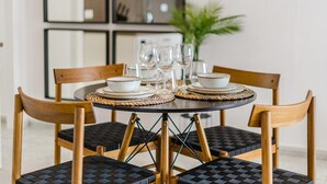 Una mesa redonda de comedor con cuatro sillas, cada una con un mantel tejido. La mesa está dispuesta con platos blancos, tazones y copas de cristal.