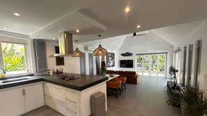 Une cuisine spacieuse dotée d’un grand îlot central, de luminaires suspendus modernes et d’un coin repas avec un canapé et des fauteuils.