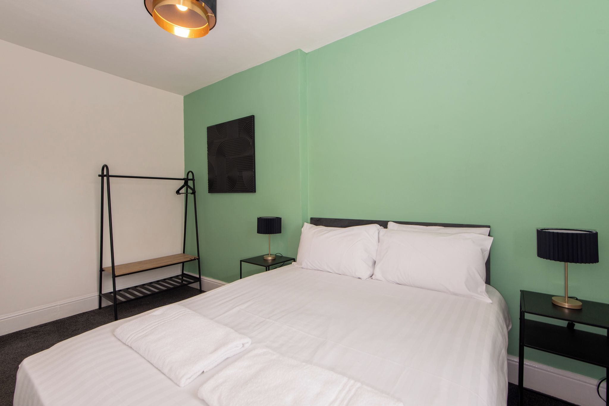 A neatly made bed with white linens, two bedside tables with lamps, a wall-mounted shelf, and a single artwork on the wall.