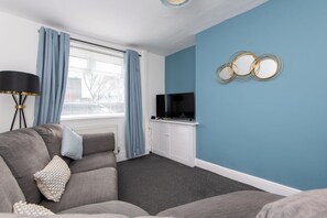 Ein modernes Wohnzimmer mit grauem Sofa, blauen Vorhängen, einem Flachbildfernseher und einer blau gestrichenen Wand.
