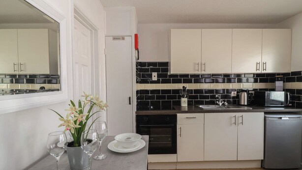 Uma cozinha moderna com armários brancos, painel de backsplash preta e branca, eletrodomésticos de aço inoxidável e uma área de refeições com pratos e copos brancos.