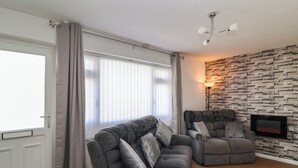 Uma sala de estar moderna com um sofá cinzento, lareira e parede com textura de pedra.