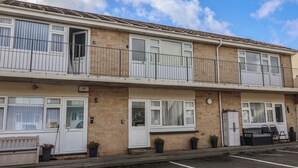 Um edifício residencial de dois andares com fachada de tijolos, janelas emolduradas de branco e varandas com grades de metal.