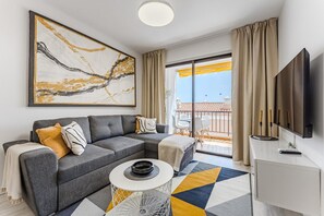 A modern living room with a grey sectional sofa, a coffee table, a flat-screen TV, and a large abstract painting. - Vacation Apartment 'Drilasol 1 Bed' with Shared Pool, Balcony and Wi-Fi (Puerto de Santiago)