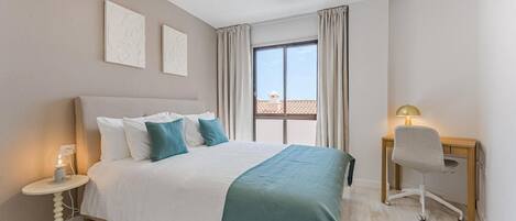 Ein Hotelzimmer mit einem Bett, einem Schreibtisch, einem Stuhl, einer Lampe und einem Vorhangfenster.