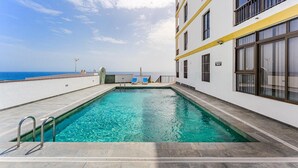Ein Pool auf dem Dach mit freiem Blick auf den Ozean, ein Gebäude mit Balkonen und eine geflieste Terrasse.