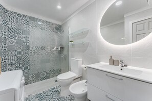 Et badeværelse med mønstrede fliser, toilet, bidet og et spejl ved håndvasken.