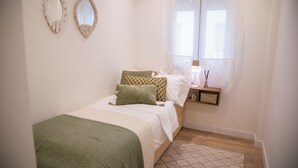 Une chambre à coucher avec un lit, deux miroirs muraux, une table de chevet avec une lampe et une fenêtre ornée de rideaux légers.