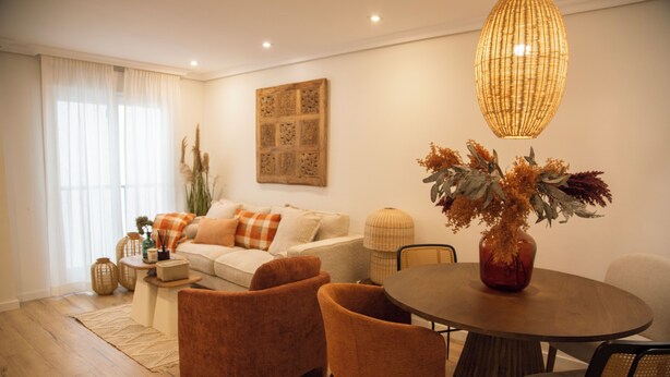 Un salon moderne comprenant un canapé, deux fauteuils, une table basse et une table à manger avec des chaises. On peut voir un vase décoratif contenant des plantes séchées sur la table.