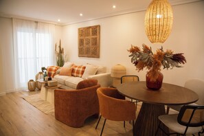 A modern living room with a sofa, two armchairs, a coffee table, and a dining table with chairs. There is a decorative vase with dried plants on the table. - Hidden Gem: GRAN TEATRO FALLA SUITES (Cádiz)