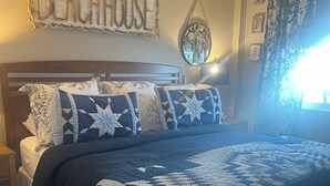 Un dormitorio con cama, mesita de noche, reloj de pared, espejo y un letrero que dice 'BEACHHOUSE'.