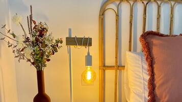 Ein Bett mit weißer Bettwäsche, ein runder Nachttisch mit Lampe und eine Vase mit Blumen.