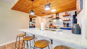 A modern kitchen with a large island, bar stools, wooden ceiling, and a herringbone-patterned backsplash. - Family condo retreat near Orlando parks (Kissimmee)