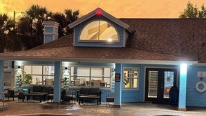 A poolside area with a covered seating area, a pool, and a building with a large arched window. - Family condo retreat near Orlando parks (Kissimmee)