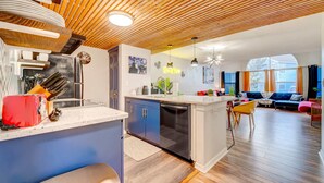 A modern kitchen with a wooden ceiling, a dining area with a blue sofa, and a view of the outside. - Family condo retreat near Orlando parks (Kissimmee)