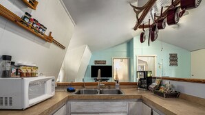 A kitchen with a microwave, sink, and wooden shelves with spices.