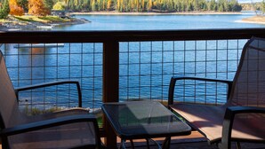 A deck with two chairs and a small table overlooking a lake with trees and a dock.