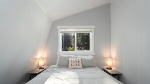 A bedroom with a bed, two bedside tables, a window, and a view of trees.