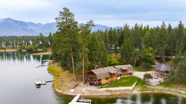 A lakeside cabin with a dock, surrounded by forest and mountains.