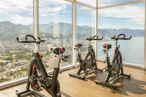 Une salle de sport équipée de vélos d’appartement et dotée d’une grande fenêtre donnant sur la ville et les montagnes.