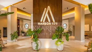 A modern hotel lobby with a large wooden reception desk, potted plants, and a sign reading "Harbor 171". - Stylish Beachfront Studio by Moikkarentals (Puerto Vallarta)