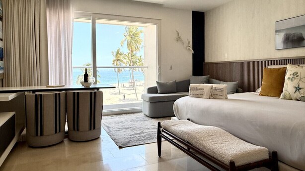 Een moderne hotelkamer met een bed, een zithoek, een eethoek en uitzicht op het strand.