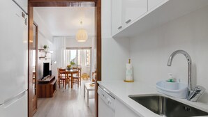 A modern kitchen with white cabinetry, a stainless steel sink, and a dining area with wooden chairs and a table.