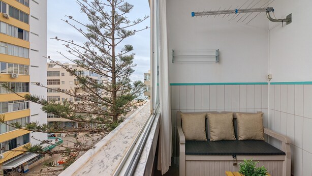 A balcony with a view of buildings, a bench with cushions, a potted plant, and a metal antenna.