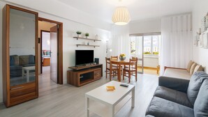 A modern living room with a flat-screen TV, wooden furniture, a dining area, and a balcony with a view.