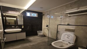 Et moderne badeværelse med et stort spejl, en hvid vask, et glasafskærmet brusebad og et toilet.