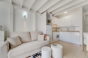 A modern living room with a sofa, two side tables, and a kitchen area with white cabinets and appliances.