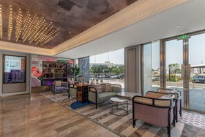 A modern lobby with seating areas, a bookshelf, and a large window offering a view of the street. - MERCURE GUANGZHOU FINANCIAL CITY (Guangzhou)