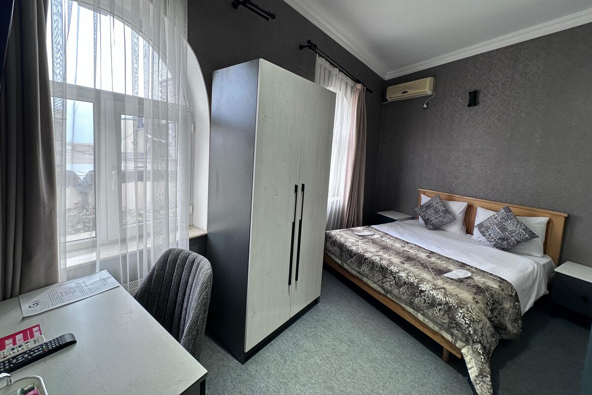 A hotel room with a bed, a desk, a wardrobe, and a window with curtains.