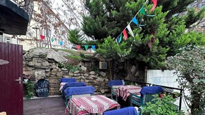 A rustic outdoor seating area with stone walls, tables with patterned tablecloths, and a variety of flags. - Heritage Old City Hotel (Baku)