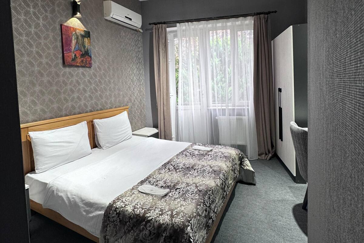 Une chambre d’hôtel avec un grand lit, une table de chevet, une chaise, une fenêtre avec des rideaux et un tableau au mur.